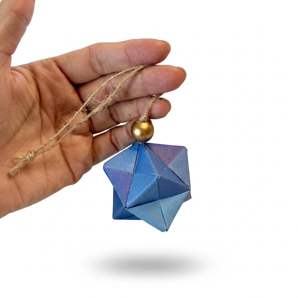Detalle de una esfera de origami azul y morada colgando de la mano, con cuenta dorada
