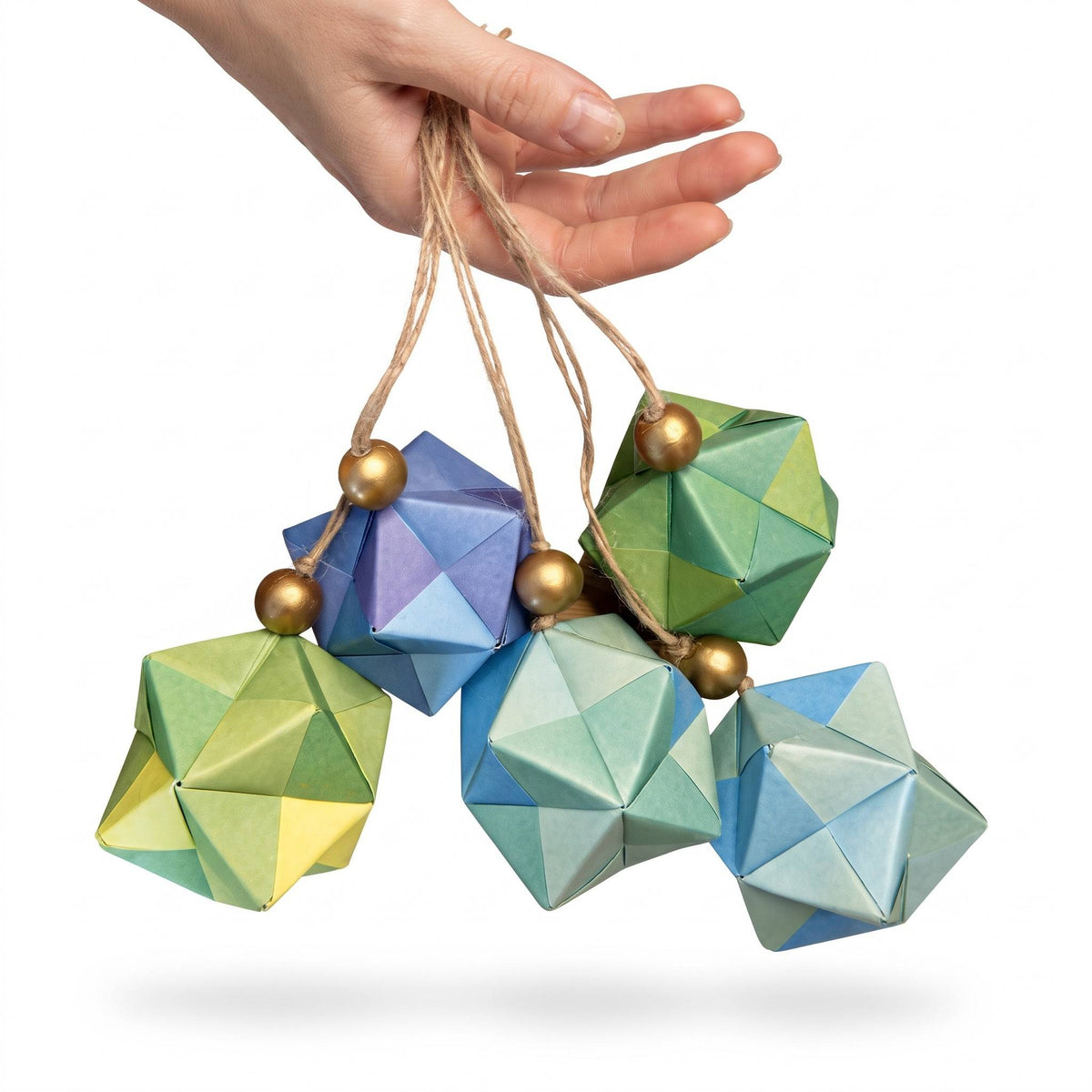 Mano sosteniendo un racimo de esferas de origami verdes y azul claro con cuentas doradas