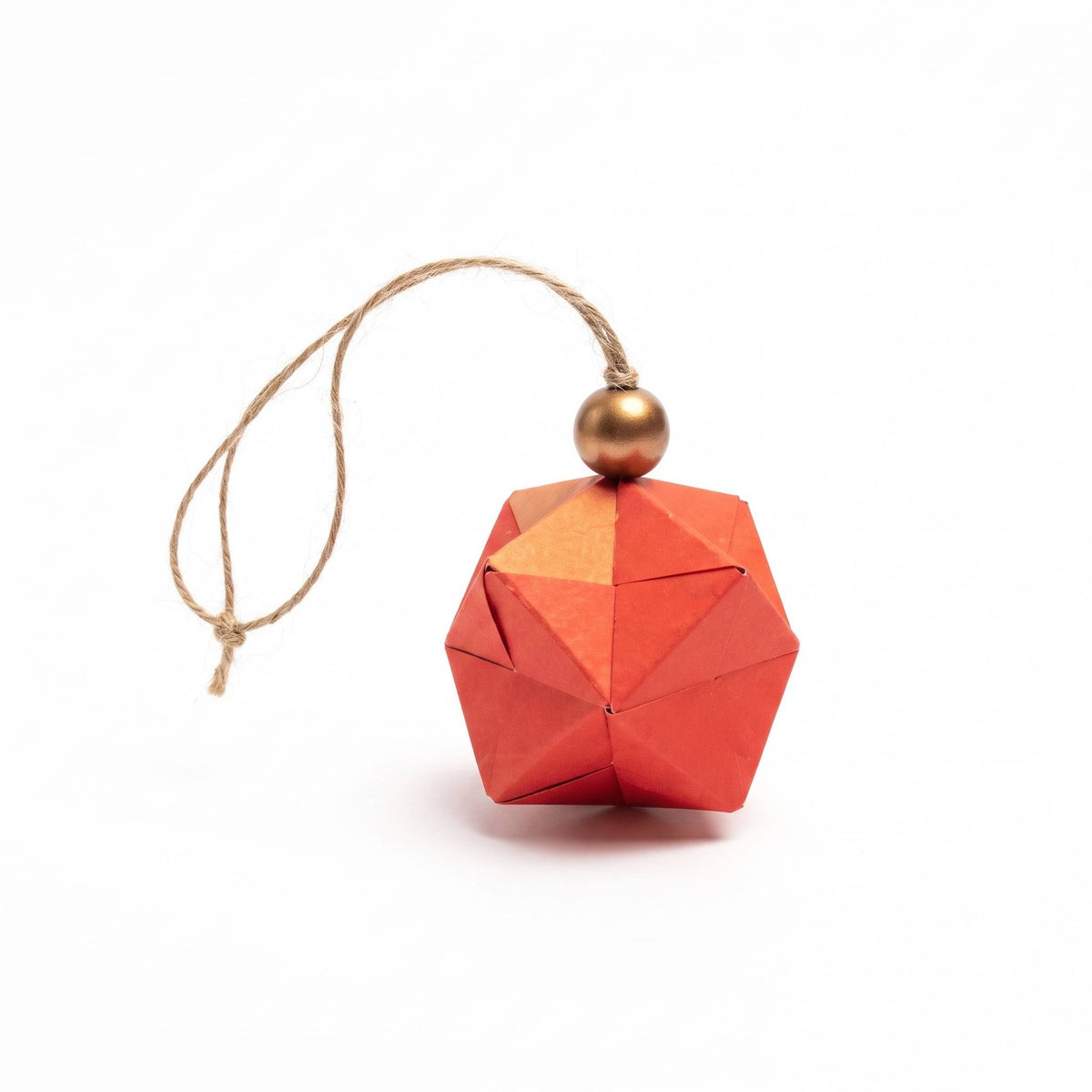 Esfera de origami naranja rojizo con cuenta dorada y cordel de yute, sobre fondo blanco