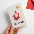 Tarjeta Feliz Navidad de origami hecha a mano con Papá Noel rojo y estrella dorada, sostenida en la mano junto a un sobre rojo